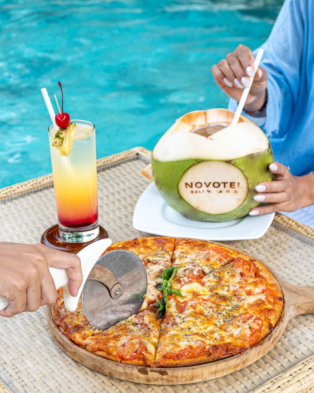 Two guests enjoying a poolside floating food pizza and coconut water in Novotel Hotel