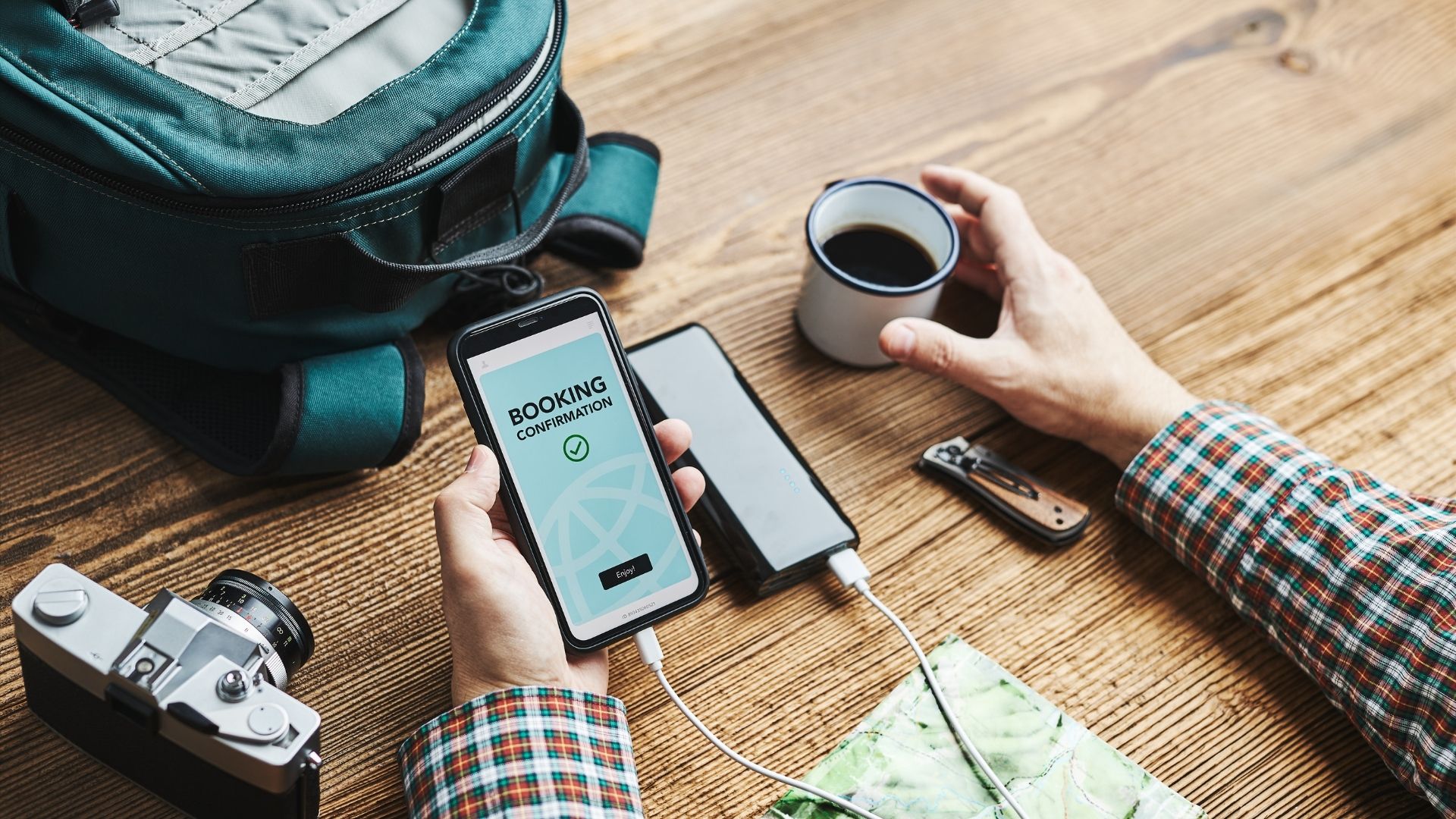 A male traveler's hand holding a phone displaying the successful hotel booking process while enjoying a cup of coffee.