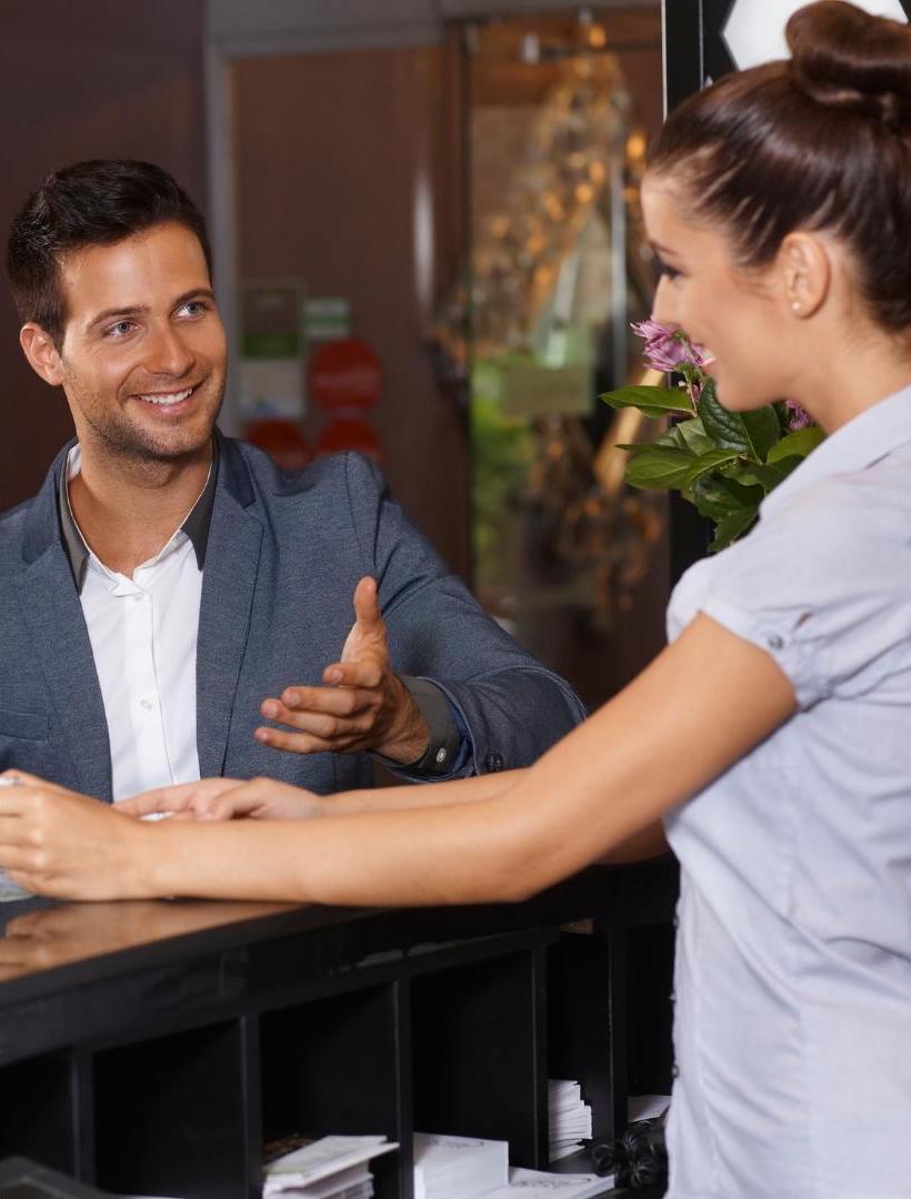 Caucasian-male-model-with-white-shirt-and-grey-suit-talking-with-the-receptionist-in-white-uniform-at-hotel-front-office-symbolic-of-hotel-guest-persona