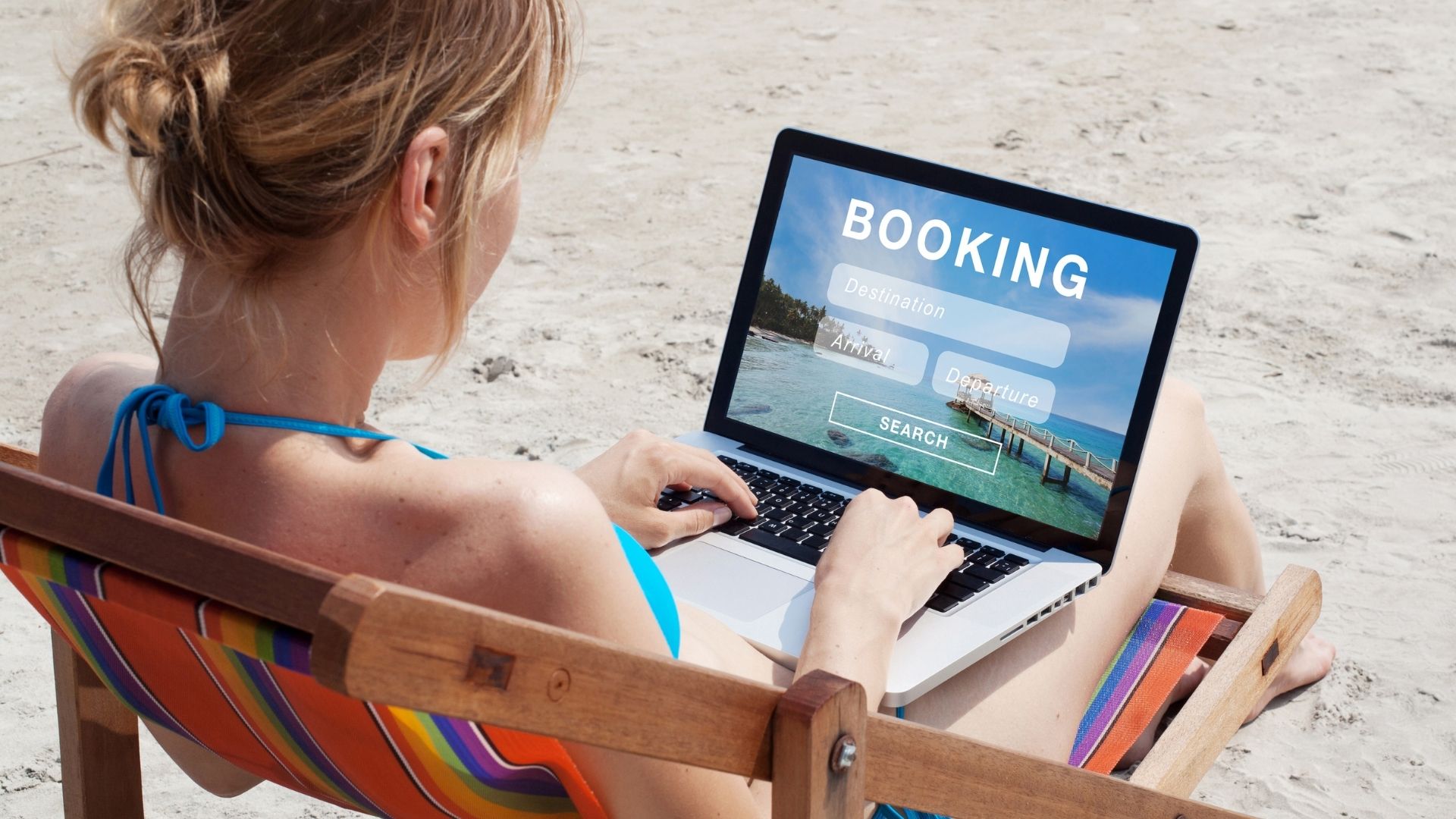 A female traveler in a beach books her hotel through an online travel agency (OTA) using her laptop.