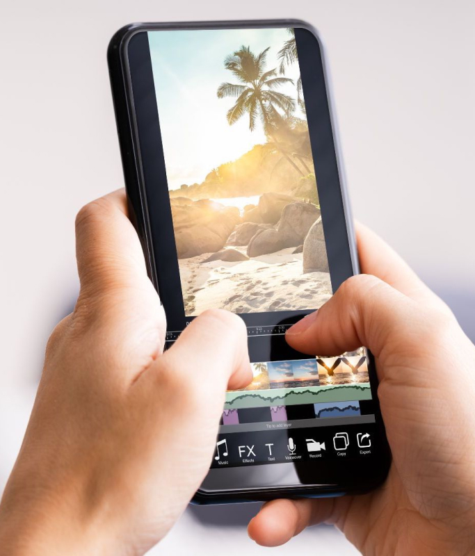 A woman with black hair tied up is sitting in the living room on a comfortable and soft sofa creating compelling content about her vacation in Bali featuring a beach with white and clean sand and coconut trees using aesthetic video editing applications VN and Capcut