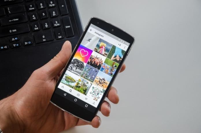 Hand of social media marketer holding a black smartphone showing client's Instagram feed