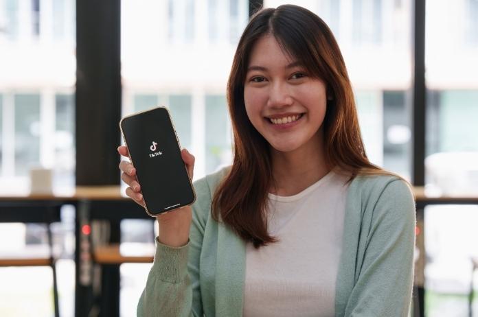 Female influencer smiling while showing her smartphone displaying TikTok logo