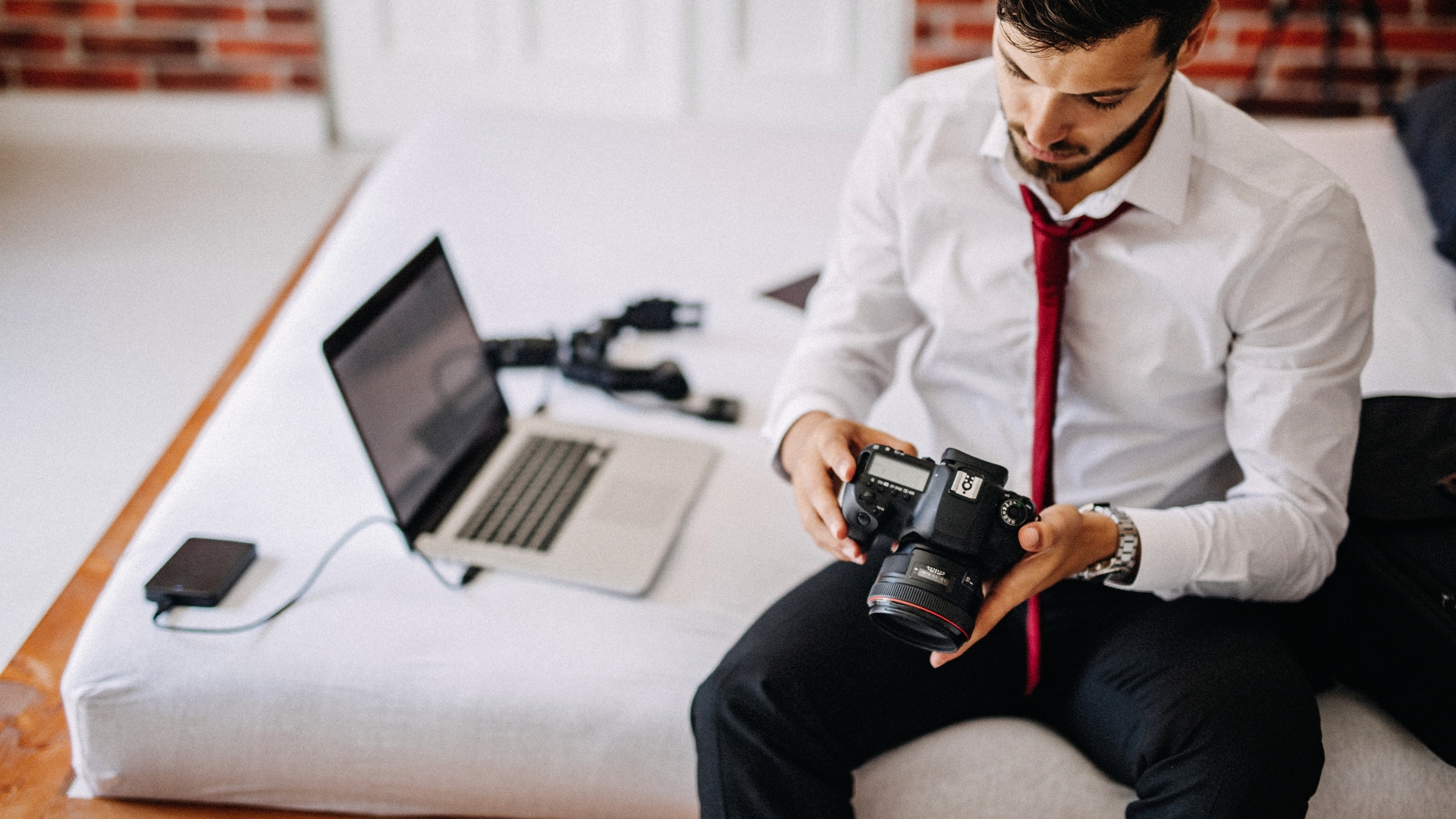 an expert photographer is doing hotel photography service with his camera with laptop next to him on hotel bed