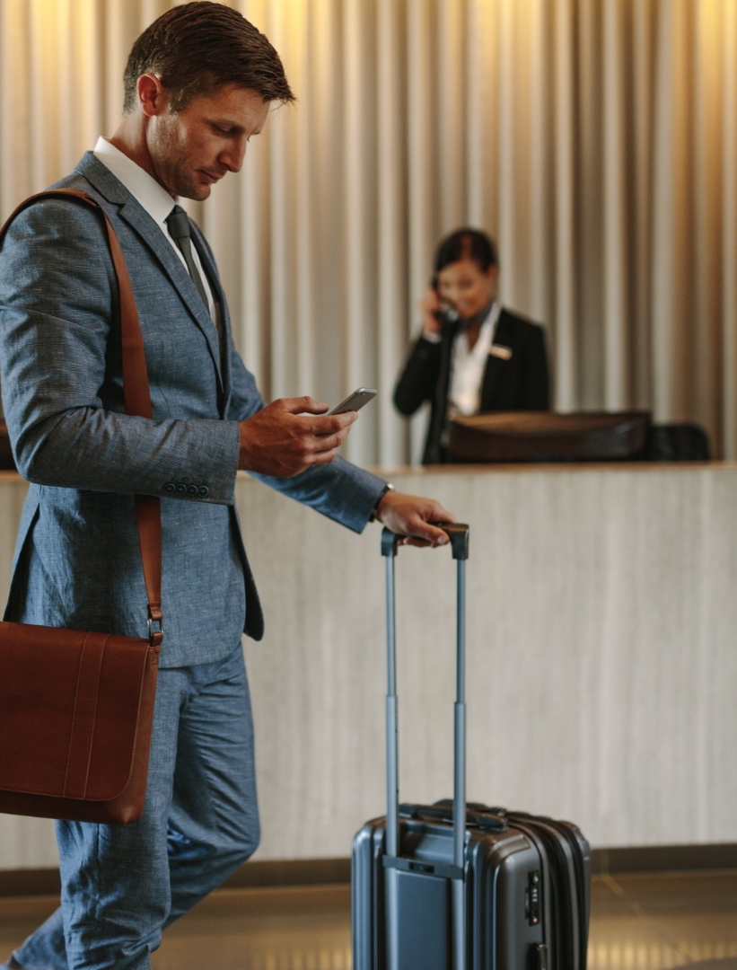 business-man-in-grey-suit-bring-his-silver-luggage-and-brown-small-bag-and-walking-in-front-of-the-hotel-reciptionist
