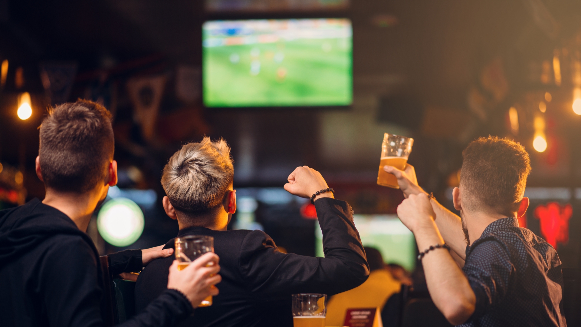 three men watching football at a bar called lucky bar day wearing black shirts and carrying beers