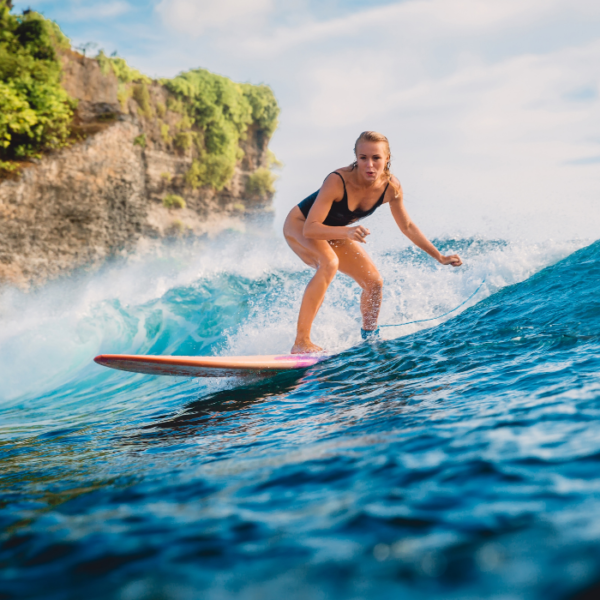 A female surfer riding the waves at Eco Beach in Pererenan, Canggu, with a white and orange surfboard and wearing a stylish black swimsuit.