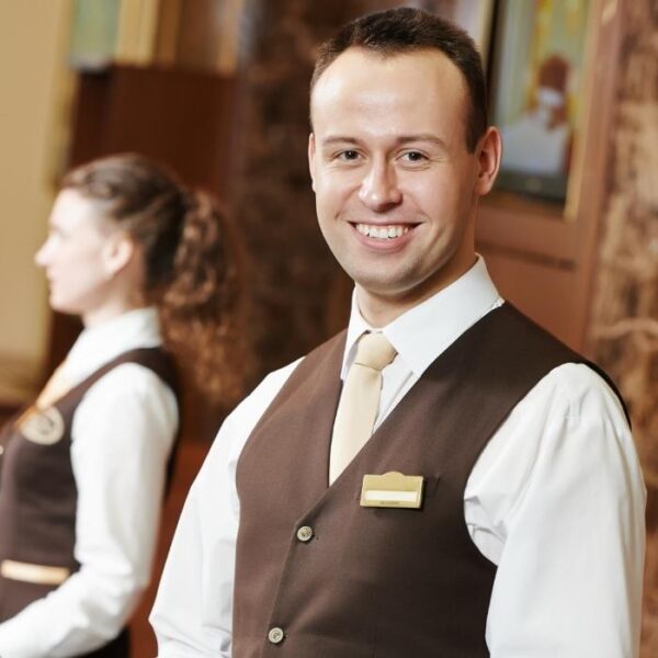 A hotel staff wearing a brown and white uniform smiles at the camera because he knows how to increase hotel revenue in Bali