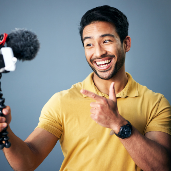 A man in a yellow polo shirt makes content for a travel agency using a white phone, a microphone, and a black tripod