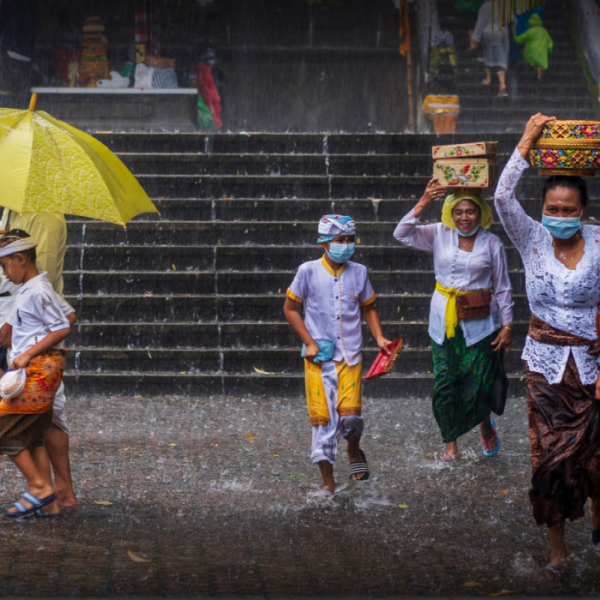 A group of Balinese people walking in the rain while the season affects the performance marketing of the hospitality business.